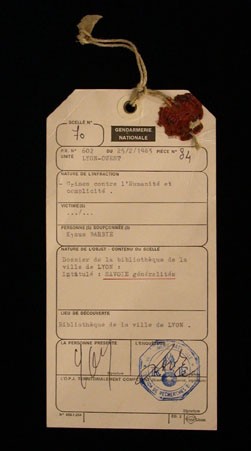 Evidence tag from the trial of Klaus Barbie in Lyon, France. This standard police form lists Barbie's infractions as crimes against humanity and complicity, concepts defined at the International Military Tribunal at Nuremberg decades earlier. The line in which the victims' names would be recorded is left blank. February 25, 1983.