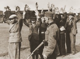 A German soldier guards a group of Poles and Jews who have been rounded-up and forced to stand in a line with their arms raised, Poland, September 1939. 