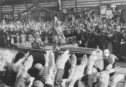 Standing in an open car, Adolf Hitler salutes a crowd in Hamburg, Germany. Photo dated August 17, 1934.