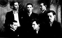 İki dünya savaşı arası dönemde Polonya’daki altı genç erkeğin grup fotoğrafı. Resimde soldan sağa, ayaktakiler: Moishe Krol, Moishe Rafilovitch ve kimliği belirsiz bir adam. Soldan sağa, oturanlar: Itzrik Rosenblat, Anschul Goldstein ve kimliği belirsiz bir adam. Krol, Rafilovitch ve Rosenblat—SS, nüfusun çoğunu Ağustos 1942’de Treblinka’ya sürdükten sonra—Polonya’nın Radom kentinde kalmaya zorlanan Yahudi terzilerdi.