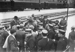 A group of Jewish men on a train platform with French policemen at the Austerlitz station before deportation to the Pithiviers internment ... [LCID: 44280]
