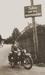 一个骑摩托车的人在读一块指示牌，上面标明：“此处不欢迎犹太人”。拍摄地点：德国，拍摄时间：大约 1935 年。