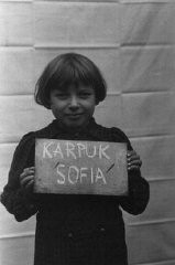Sofia Karpuk holds a name card intended to help any of her surviving family members locate her at the Kloster Indersdorf displaced persons camp. This photograph was published in newspapers to facilitate reuniting the family. Kloster Indersdorf, Germany, October-November 1945. 
 