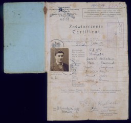 Inside pages of a citizenship certificate with the innermost paper unfolded at the bottom. The cover is light blue. The printed text and handwritten notes are both in Polish. A photograph of a man with short dark hair and a light skin tone is present in the top left hand corner of the certificate.