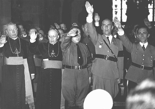 <p>Catholic clergy and Nazi officials, including Joseph Goebbels (far right) and Wilhelm Frick (second from right), give the Nazi salute. Germany, date uncertain.</p>
