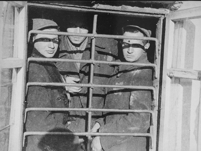 Scene photographed by George Kadish: Jewish prisoners behind a barred window in the Kovno ghetto jail.