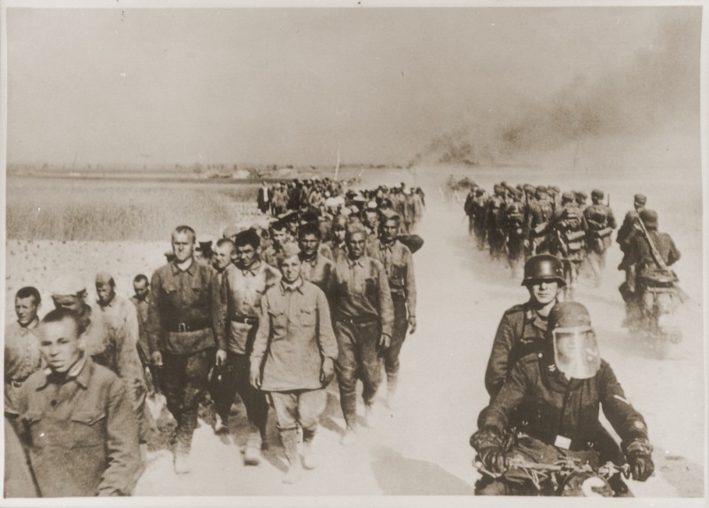 At left, a column of Soviet prisoners of war, under German guard, marches away from the front.