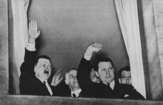 Adolf Hitler, Wilhelm Frick, and Hermann Goering wave to a torchlight parade in honor of Hitler's appointment as chancellor.