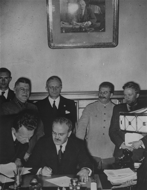 Soviet foreign minister Viacheslav Molotov signs the German-Soviet pact as Soviet leader Joseph Stalin (white uniform) and German foreign minister Joachim von Ribbentrop (behind Molotov) look on.
