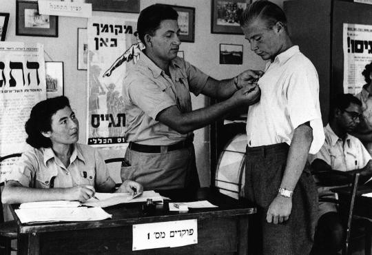 In the British army recruitment office in Tel Aviv, an official pins the symbol of the volunteer Jewish Brigade onto the shirt of ... [LCID: 11165]