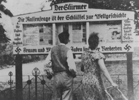 A German couple reads an outdoor display of the antisemitic newspaper "Der Stuermer" ("The Attacker"). [LCID: 66674]