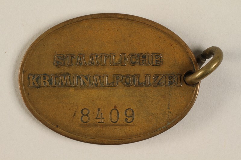 Official identification tag (warrant badge) for the Criminal Police (Kriminalpolizei or Kripo), the detective police force of Nazi Germany. This side reads: Staatliche Kriminalpolizei (State Criminal Police) and identifies the officer's number as 8409.
 
 
 