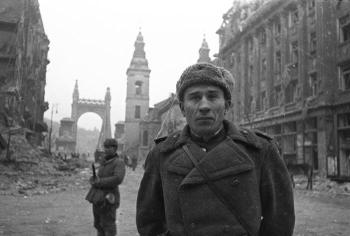 Portrait of a Soviet soldier standing on a heavily damaged street in Budapest