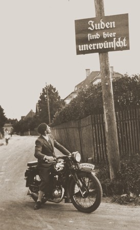 A motorcyclist reads a sign stating "Jews are not welcomed here." [LCID: 97470]