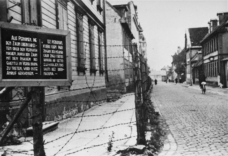 <p>Tábla német és lett felirattal, amely arra figyelmeztet, hogy a kerítést átlépő vagy a rigai gettó lakóival kapcsolatot létesítő személyeket lelövik. Riga, Lettország, 1941–1943.</p>