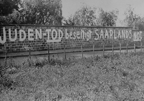 Antisemitic graffiti painted on the wall of a Jewish cemetery reads "The death of the Jews will end the Saarland's distress." [LCID: 73939]