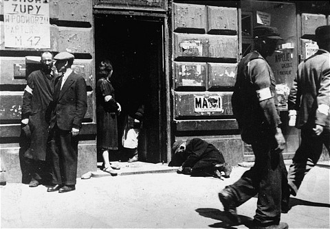 Street scene in the Warsaw ghetto. The sign at left announces: "Soup in the courtyard, first floor, apt.