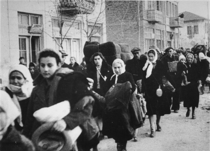 Jewish deportees from Macedonia march along a street in Skopje carrying their belongings. Skopje, [Macedonia] Yugoslavia, March 1943. 

The Jews of Bulgarian-occupied Thrace and Macedonia were deported in March 1943. Between March 4 and March 9, the 4,219 Jews from Thrace were rounded-up and concentrated in the two towns of Gorna Dzumaya and Dupnitsa. Two weeks later, between March 19 and March 21, they were transported in two trains to the port of Lom on the Danube. From Lom they were loaded onto four Bulgarian ships and taken to Vienna, where they were once again put on trains bound for Treblinka. On March 11, over 7,000 Macedonian Jews from Skopje, Bitola, and Stip were also rounded-up and assembled at the Tobacco Monopoly in Skopje, whose several buildings had been hastily converted into a transit camp. The Macedonian Jews were kept there between eleven and eighteen days, before being deported by train in three transports between March 22 and 29, to Treblinka. None of those deported from the Tobacco Monopoly survived.