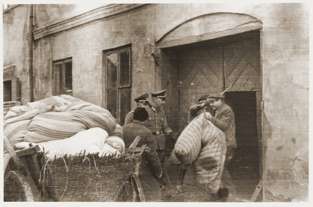 A member of the German Order Police raises a stick to beat a Jew who is loading his bundles onto a wagon during the expulsion from Sieradz in German-occupied Poland. Photo dated 1940–1942.