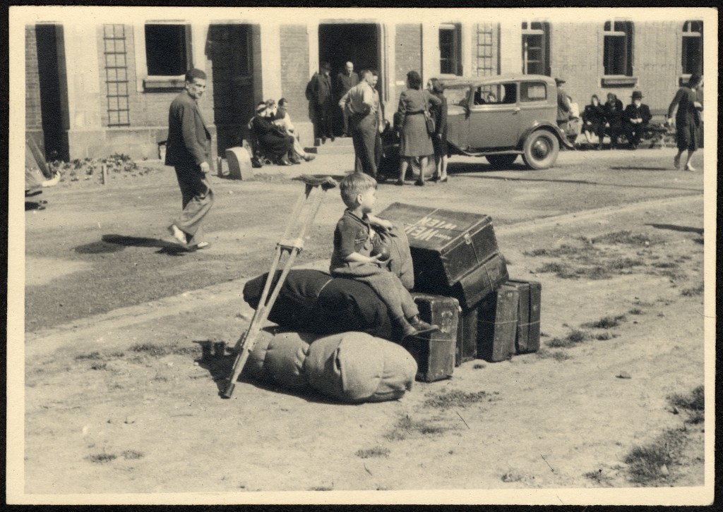 A young child sits among luggage while waiting to depart the Deggendorf displaced persons camp. [LCID: 22582]