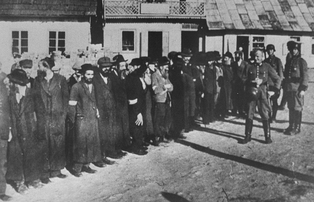 Members of the German Order Police stand guard over a group of orthodox Jewish men, 1942. The men have have been rounded-up either for forced labor or public humiliation. Krakow, in German-occupied Poland.