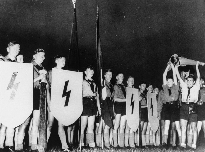 <p>A Hitler Youth ceremony, typical of those conceived by Baldur von Schirach. They aimed to strengthen dedication to Hitler. Members recited verses, sang patriotic songs, and performed "mock funerals" for "fallen comrades." Germany, date uncertain.</p>