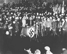 وزير الدعايات يوزف جوبلس (خلف منصة) يشجع الطلاب وأعضاء جيش الإنقاذ لحرق الكتب التي تعتبر "غير ألمانية" خلال حرقها في ساحة أوبرنبلاتس ببرلين, ألمانيا. 10 مايو 1933.