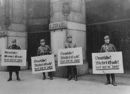 رجال SA أمام محل مملوك لليهود يقومون بتنبيه بالمقاطعة بالعلامات التالية ' أيها الألمان! دافعوا عن أنفسكم! لا تشتروا من اليهود! ' برلين، ألمانيا، 1 أبريل 1933.