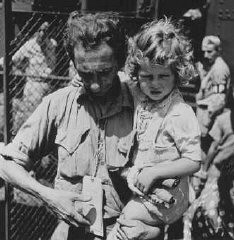 Jewish refugees from Europe arrive at the emergency refugee shelter at Fort Ontario, in the United States. A father, holding his daughter, checks his tags. Oswego, New York, United States, August 4, 1944.