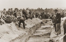 Au cours de l'inhumation publique, les parents des défunts et les habitants des environs jettent de la terre dans la fosse commune des victimes du pogrom de Kielce.