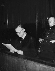 El acusado Alfred Rosenberg, el antiguo jefe ideólogo del Partido nazi, lee un documento durante el juicio a los criminales de guerra del Tribunal Militar Internacional de Núremberg. Detrás de él se encuentra su codemandado, general Alfred Jodl, anteriormente el jefe del Estado Mayor para el Ejército. Núremberg, Alemania, 1945-1946.
