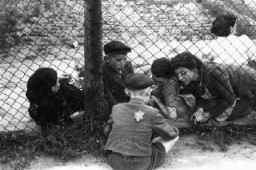 Родственники прощаются с ребенком через ограду центральной тюрьмы гетто, где детей, больных и стариков держали перед депортацией в Хелмно во время операции "Gehsperre" (нем. — "путь на плаху"). Лодзь, Польша, сентябрь 1942 года.