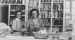 Two German Jewish refugee women stand behind the counter of the Elite Provision Store (delicatessen) in Shanghai. Pictured on the left is the owner, Gerda Harpuder; on the right is her cousin Kate Benjamin. In 1939 Hans and Gerda Harpuder sold their crystal, silver, and other family possessions shipped from Berlin in order to open a grocery store in Hongkew at 737 East Broadway.