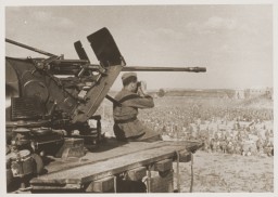 A German guard sitting on the end of a 20mm gun platform watches over 50,000 Soviet Prisoners of War (POWs) at Stalag 349, Ukraine, August 14, 1941.