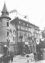 German citizens stand outside the decorated Hotel Dreesen, where Neville Chamberlain and Hitler held their second meeting on the Sudetenland and German demands for Czech territory.  Nazi flags and the Union Jack fly from the building. Bad Godesberg, Germany, September 22, 1938.