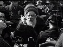 Huge crowds of well wishers gather in the streets on the occasion of the wedding of the Munkács rabbi's 18-year-old daughter, Frime Chaye Rivke. The Grand Rabbi of Munkács (Mukacevo), Chaim Elazar Shapiro, father of the bride, makes a speech in Yiddish exhorting Jews in America to continue to keep Shabbes (to observe the sabbath day). The wedding party then enters the synagogue grounds, and the cantor sings blessings beneath the wedding canopy. The wedding concludes with festive klezmer music. The marriage had been arranged six years earlier, though the bride and groom did not meet until their wedding day. Newspaper accounts indicate that some 20,000 people attended the celebrations.