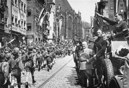Members of the Hitler Youth march before their leader, Baldur von Schirach (at right, saluting), and other Nazi officials including Julius Streicher. Nuremberg, Germany, 1933.