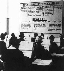 Γερμανίδες εν ώρα εργασίας στα γραφεία της Γερμανικής υπηρεσίας απογραφών. Στον πίνακα περιλαμβάνονται οδηγίες για την πινακοποίηση: στην κεντρική στήλη δίδεται η οδηγία ότι ο αριθμός 3 είναι η ένδειξη που πρέπει να χρησιμοποιείται για τους Εβραίους. Γερμανία, 1933.