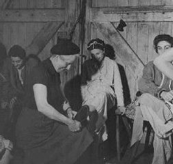 Soon after liberation, a British woman helps a camp survivor try on shoes. Bergen-Belsen, Germany, after May 1945.