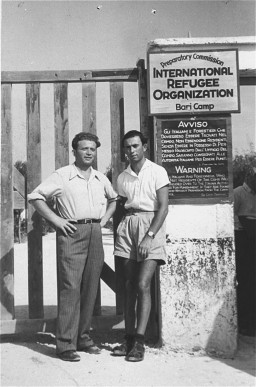 Abraham Morgenstern, right, stands in front of a sign marking the entrance to Bari Transit displaced persons (DP) camp in Italy, circa July 1947.