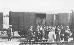 Le personnel SS mène la garde tandis que la police du ghetto de Lodz fait monter des Juifs à bord d’un train de déportation pour Chelmno ou Auschwitz. Lodz, Pologne, entre mai et août 1944.