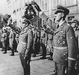 Reinhard Heydrich (right) and his deputy, Karl Hermann Frank (center), stand at attention during Heydrich's inauguration as governor ... [LCID: 64053]