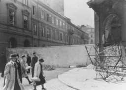 Polish civilians walk by a section of the wall that separated the Warsaw ghetto from the rest of the city. Warsaw, Poland, 1940–41.