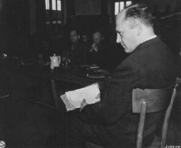 Friedrich Hoffman, une pile de certificats de décès dans la main, témoigne du meurtre de 324 prêtres catholiques exposés à la malaria durant les expériences médicales menées par les Nazis dans le camp de concentration de Dachau. Dachau, Allemagne, 22 novembre 1945.