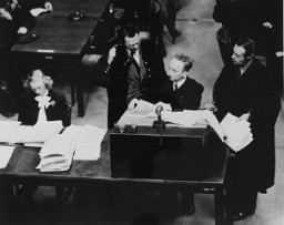 Chief Prosecutor Benjamin Ferencz presents evidence during the Einsatzgruppen Trial, Case #9 of the Subsequent Nuremberg Proceedings. Ferencz is flanked by German defense lawyers Dr. Friedrich Bergold (right, counsel for Ernst Biberstein) and Dr. Rudolf Aschenauer (left, counsel for Otto Ohlendorf), who are protesting the introduction of certain documents as evidence.