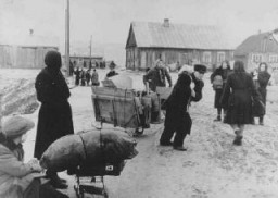 Jews forced into the Kovno ghetto move their belongings into the ghetto. In the center, a man is pulling a disassembled wardrobe. He was never able to put it together because of the crowded conditions in the ghetto. Clothes were often hung from nails in the wall instead. Lithuania, ca. 1941-1942.