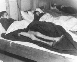 Two emaciated female Jewish survivors of a death march lie in an American military field hospital in Volary, Czechoslovakia. Pictured on the left is seventeen-year-old Nadzi Rypsztajn.The original caption reads "This girl, only seventeen years old, was forced to march 18 miles a day for 30 days on one bowl of soup a day. The 5th Infantry Division of the U.S. Third Army found 150 in the same condition when they entered Volary, Czechoslovakia."