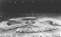 At a rally, members of the Hitler Youth parade in the formation of a swastika to honor the Unknown Soldier. [LCID: 85513]