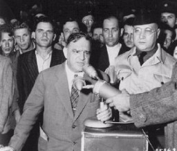 L’ancien maire de New-York Fiorello H. La Guardia, lors d’une visite des camps de l’UNRRA (Administration des Nations Unies pour les secours et la reconstruction) en Europe, parle à des survivants. Camp de personnes déplacées de Duppel. Allemagne, 20 août 1946.