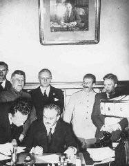 Le ministre soviétique des Affaires étrangères Viacheslav Molotov signe le pacte germano-soviétique tandis que le dirigeant soviétique Joseph Staline (en uniforme blanc) et le ministre allemand des Affaires étrangères Joachim von Ribbentrop (derrière Molotov) regarde. Moscou, Union soviétique, 23 août 1939.